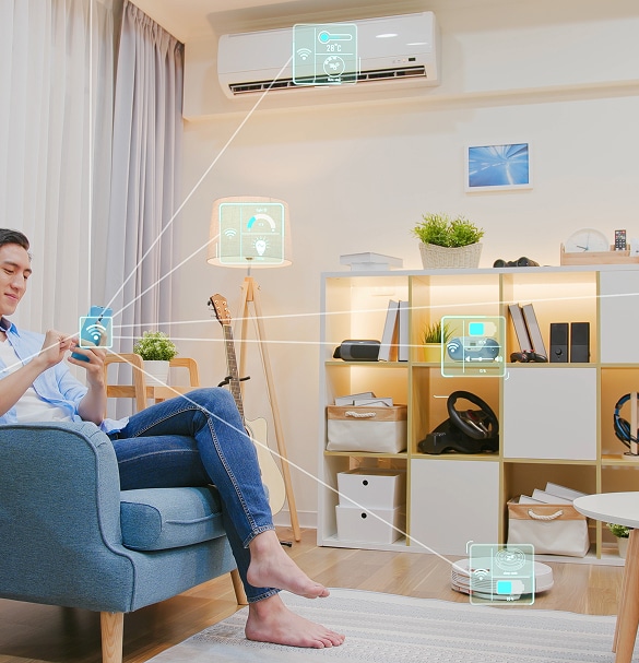 Homme contrôle une maison connectée via smartphone. Des icônes d'AC (28°C), lampe, système audio et robot aspirateur indiquent la domotique.