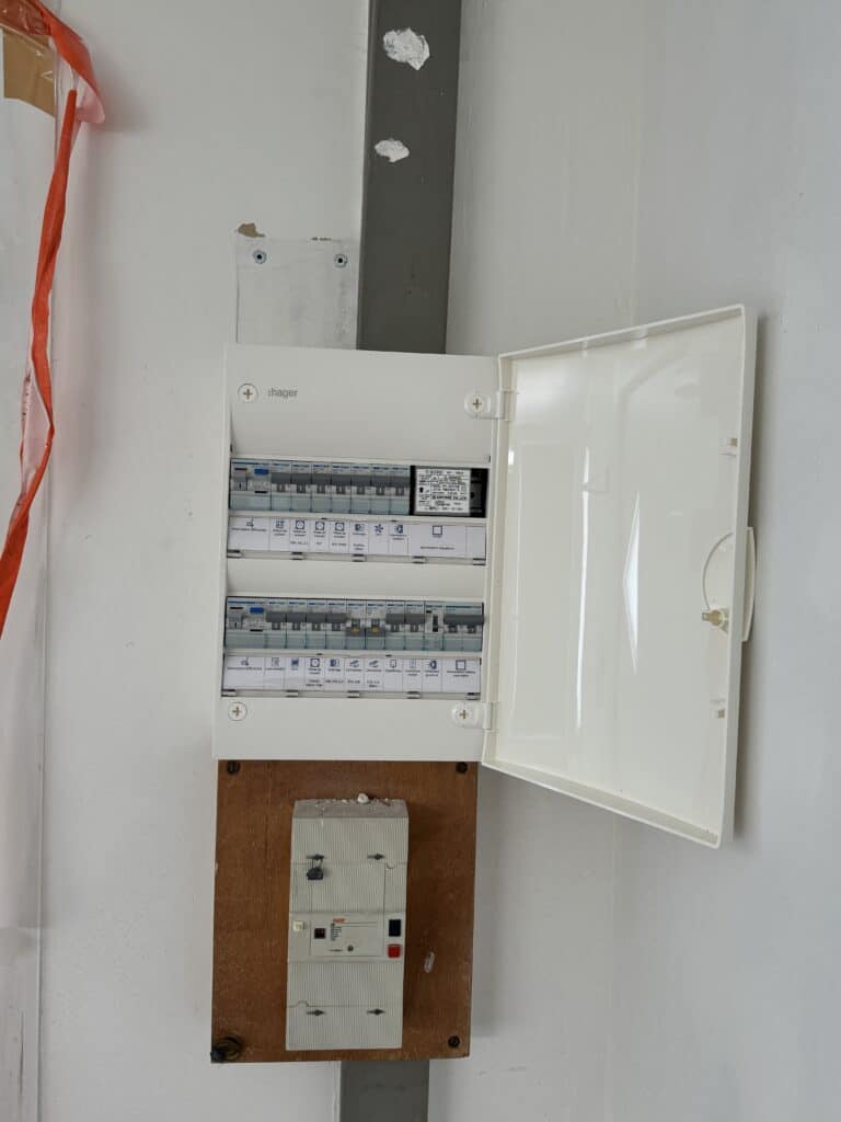 Tableau électrique Hager ouvert, montrant disjoncteurs étiquetés et module Aiphone. Disjoncteur principal Gindy DB sur support bois.